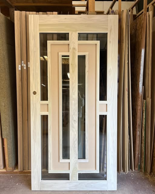 Wood and glass door with a nested rectangular pattern, standing among other door frames in a workshop